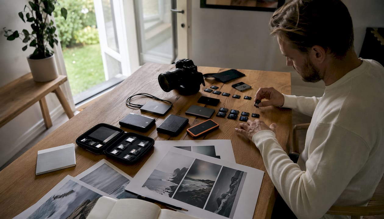 Ett skrivbord med en Nikon-kamera och olika digitala lagringsenheter.